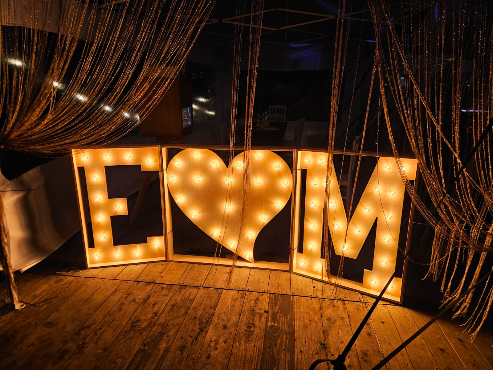 Verlichte initialen E en M met een lichtgevend hart bij een trouwfeest